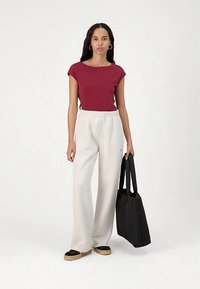 Maroon fitted t-shirt, white loose-fitting tapered pants, black tote bag, and black slip-on shoes with tan soles; simple design, soft textures.