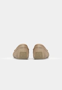 Beige semskede slip-on sko med avrundet form, teksturerte sider og gummisåler. Diskré merkevare på hælene og glatt overflate.