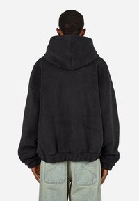 Felpa con cappuccio nera in pile, dotata di un grande cappuccio, polsini ed orlo elastici. Tessuto morbido, vestibilità oversize e cuciture prominenti sulle spalle.