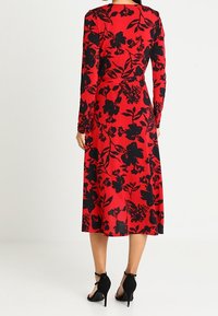 Röd blommig klänning med långa ärmar, svart blommönster, midilengd, åtsittande midja, texturerad tyg, parat med svarta högklackade skor.