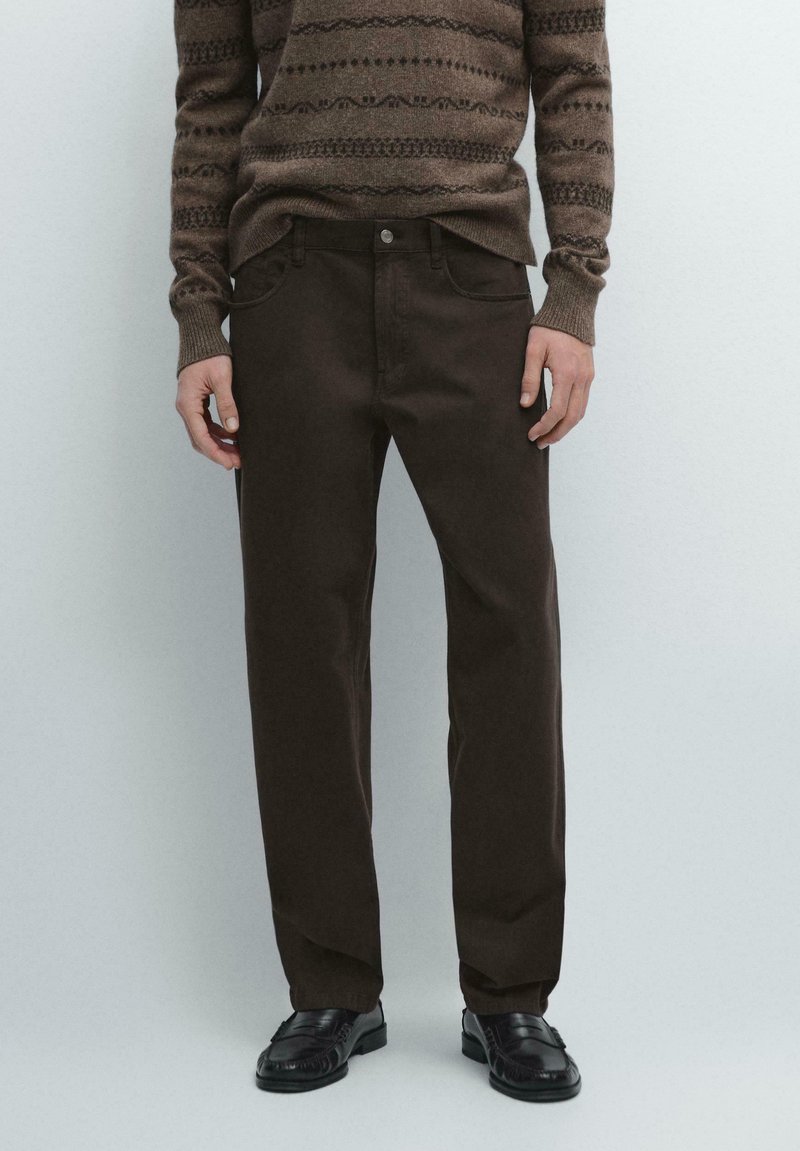 Brune bomulds denimbukser med lige ben, der har forlommer og knaplukning, kombineret med en brun mønstret sweater.