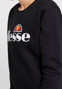 Sudadera negra con cuello redondo, que presenta un logotipo blanco prominente y un gráfico semicírculo colorido en la parte superior. Textura suave.