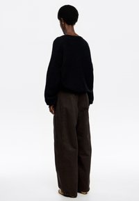 Suéter negro de corte holgado y hombros caídos, combinado con pantalones de pierna ancha de color marrón oscuro. Textura suave, diseño minimalista y sin patrones visibles.