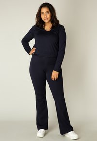 Navy lange mouwen top en bijpassende flared broek van zacht materiaal, met een ronde hals en aansluitende pasvorm, gecombineerd met witte sneakers.