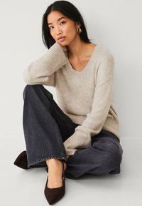 Beige wollen blend trui met een V-hals en geribbelde manchetten, gecombineerd met donkere denim wijde broek en bruine suède hakken.