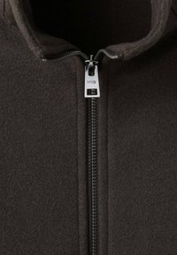 Tmavosivá flísová bunda s vysokým golierom a predným zipsom. Má strieborný jazdec so značkou a zvýrazňuje hladkú textúru.