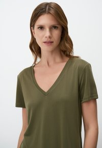 T-shirt verde oliva a V in morbido tessuto, con maniche corte e vestibilità comoda. Texture liscia senza motivi o accenti visibili.