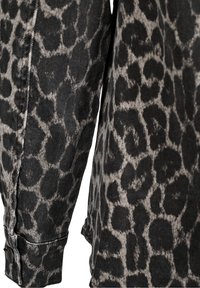 Schwarzer Denim-Stoff mit einem grauen Leopardenmuster; zeigt ein Detail mit Knopfmanschette und eine Nahaufnahme des Ärmels.