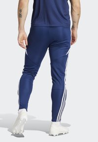 Marineblauwe sportbroeken met witte zijkanten, gemaakt van een soepele, rekbare stof. Heeft een aansluitend ontwerp en taps toelopende benen.