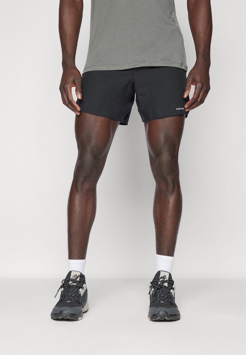 Black athletic shorts with a smooth texture, paired with a gray short-sleeve shirt and black running shoes with white accents and laces.
