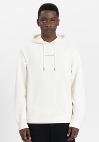 Weißer Kapuzenpullover mit einer Fronttasche, versehen mit einem kleinen goldenen "TOMORROWLAND"-Logo. Weicher Stoff, lockere Passform und gerippte Bündchen.