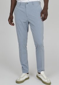 Světle modré kalhoty vyrobené z texturované tkaniny, s knoflíkovým zapínáním, bočními kapsami a slim fit, doplněné bílými a zelenými teniskami.