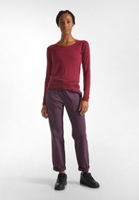 Camicia bordeaux a maniche lunghe abbinata a pantaloni viola larghi arrotolati e sneakers nere. Tessuto morbido con una vestibilità casual.