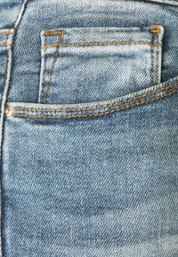 Ljusblå denimficka med kontrasterande orange sömmar, en liten silvernitet och ett texturerat tyg med en blekt utseende.