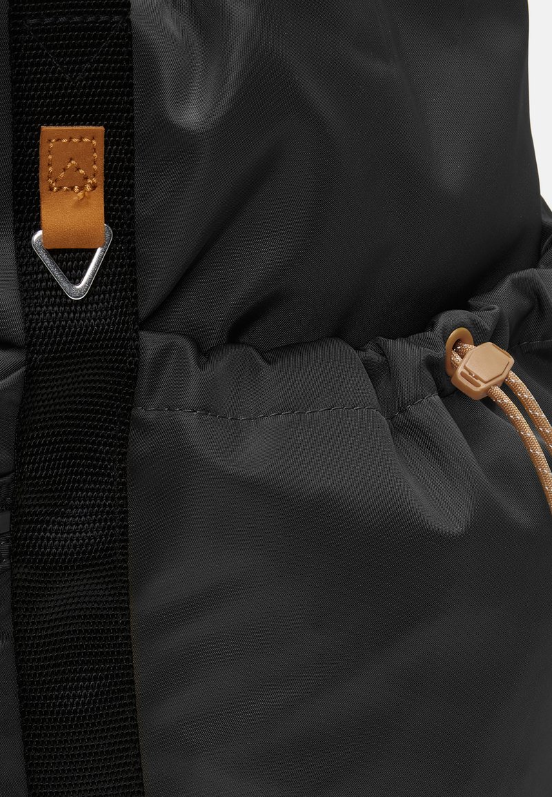 Zaino nero caratterizzato da un tessuto testurizzato, chiusura a cordoncino con accenti beige e una clip metallica, che mette in risalto il contrasto tra i materiali.