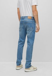 Světle modré slim džíny s kapsami na zadní straně, koženou značkovou nášivkou a kontrastním prošíváním. Nošeny s béžovými teniskami.