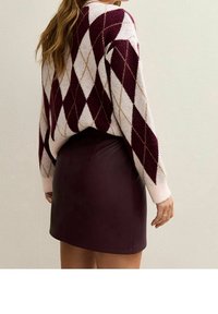 Pull en tricot avec un motif argyle bordeaux et blanc, associé à une jupe ajustée taille haute en similicuir bordeaux.