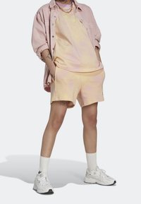 Pudrově růžová oversized košile přes odpovídající tílko a kraťasy. Bílé sportovní boty s texturovanou podrážkou a krátké bílé ponožky. Stříbrné řetízkové detaily.