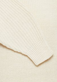 Pull en maille couleur crème avec poignets côtelés et surface texturée, présentant un design décontracté et un tissu doux.
