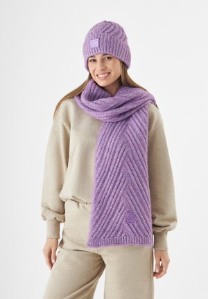 Ensemble bonnet et écharpe tricotés violets avec une texture côtelée et un motif diagonal. L'écharpe comporte une patch logo près de l'extrémité.