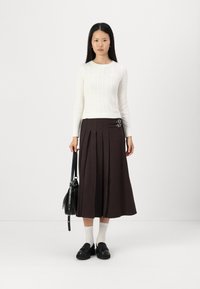 Cream ribbed sweater and brown pleated skirt with buckle accents, paired with black shoes and a black bag. White socks complement the outfit.