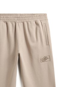 Beige sweatpants med elastisk talje, sidelommer og broderet mærkelogo på venstre lår. Blødt, tekstureret stof.