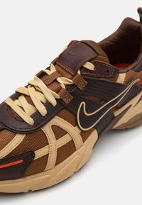 Bruna och tan sneakers i mesh och lädermaterial, med platta snören, texturerade detaljer och en framträdande Nike-logga på sidan.