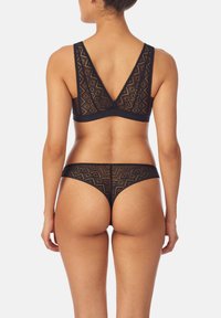 Set di lingerie in pizzo nero con motivo geometrico, reggiseno con scollatura a V profonda sul retro e spalline larghe, e perizoma abbinato a vita bassa.