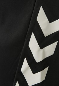 Svart tyg med iögonfallande vita chevronmönster. Slät textur med en lätt lyster som framhäver en modern atletisk design.