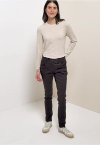 Světle šedé tričko s dlouhým rukávem v kombinaci s tmavými slim-fit kalhotami a bílými teniskami s béžovými a modrými akcenty.