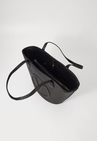 Sac fourre-tout en cuir noir avec surface texturée, ouverture supérieure, double poignées, poche intérieure zippée et logo embossé sur le côté.