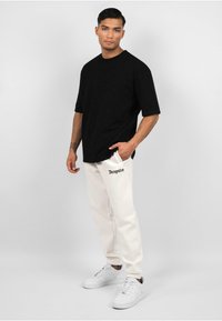 Sort oversized t-shirt, creme sweatpants med "Dropsize" tekst og hvide sneakers. Glat tekstur; afslappet, løs pasform.
