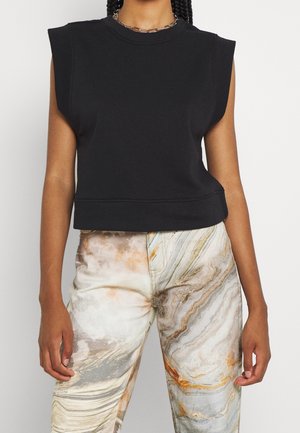 Osoba ubrana w bezrękawnikową czarną bluzkę z wyściełanymi ramionami oraz beżowe spodnie z wirującym, marmurkowym wzorem.