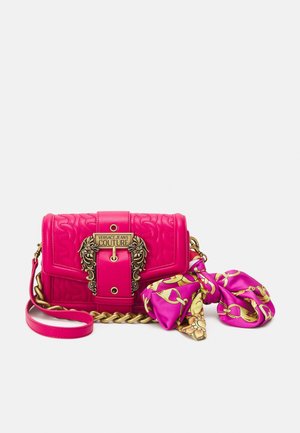 Jasnoróżowa torebka Versace Jeans Couture z ozdobnym paskiem z złotego łańcuszka, dekoracyjną złotą klamrą i dołączonym różowo-złotym apaszkiem w wzory.