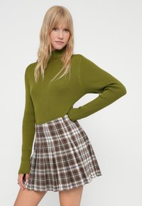 Zeleni rebrasti turtleneck pulover uparen s kariranim mini suknjom u smešnim, belim i crnim tonovima. Tkanina izgleda mekano s prilagođenim siluetom.