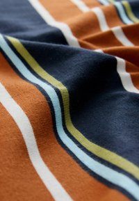 Švelnus audinys su horizontaliomis juostelėmis oranžinės, tamsiai mėlynos, baltos, šviesiai mėlynos ir žalios spalvų. Tekstūruotas mezgimas su lygiomis ir kontrastingomis spalvomis.