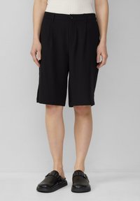 Schwarze maßgeschneiderte Shorts mit flacher Vorderseite, Knopfverschluss und seitlichen Taschen, die bis zur Mitte des Oberschenkels reichen. Glatter Stoff mit sauberen Abschlüssen.