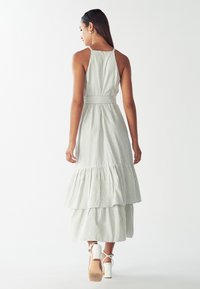 Šviesiai žaliai ir baltai raštuota suknelė be petnešų, su sluoksniuota sijonu ir prigludusia liemene. Pagaminta iš lengvo, plazdančio audinio.