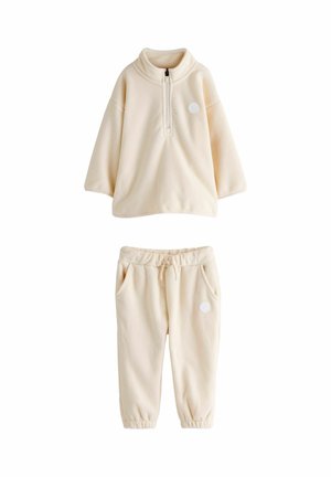 Ensemble de loungewear en polaire crème comprenant un pull à zip demi-lourd avec col montant et un pantalon assorti avec une taille élastique et des poches latérales.