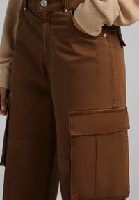 Bruna cargobyxor i mjukt tyg, med en sidoficka, bältesöglor och en framknäppning med metallisk detalj.