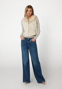 Kremas dirbtinio kailio liemenė su aukštu apykakle ir siuvinėtu raštu, derinama su aukštu juosmeniu, plačiomis mėlynomis džinsinėmis kelnėmis. Paprastų auksinių akcentų ant avalynės.