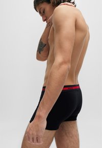 Schwarze Boxer-Shorts mit einem roten Logo-Bund, aus dehnbarem Stoff, mit einem engen Schnitt und glatter Textur.