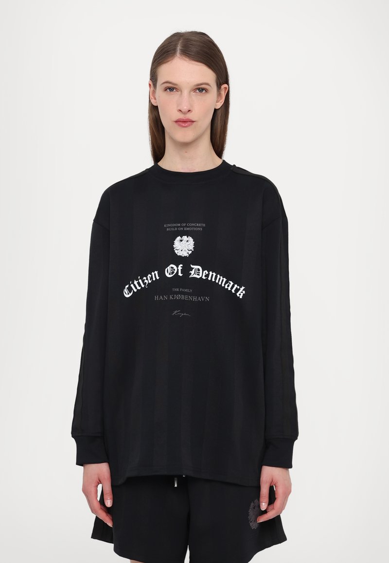 Black long-sleeve shirt with a crew neck, featuring a graphic print in white text. Striped texture. Paired with black shorts.