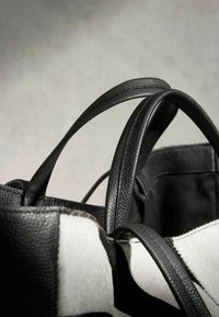 Sac cabas en cuir noir et blanc avec double poignée, montrant la texture détaillée et les coutures sur les anses et les panneaux extérieurs.
