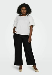 Balta tekstūruota trumpa rankovė viršutinė dalis derinama su plačiomis juodomis kelnėmis. Minimalistinis dizainas su laisvu siluetu ir subtiliomis medžiagos detalėmis.