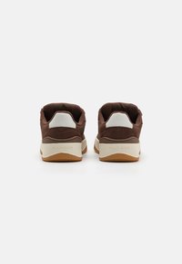 Brune sneakers med et strukturert stoffoverdel, hvite detaljer, en polstret såle og preget merkevare på baksiden. Lavt design.
