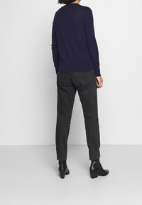 Dunkelblaue Strickjacke mit langen Ärmeln, geripptem Saum, kombiniert mit schwarzen, hochgeschnittenen Jeans und schwarzen Stiefeletten mit Blockabsatz.