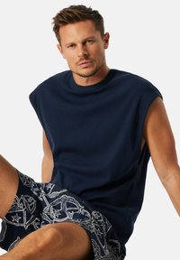Marineblauwe mouwloze shirt met een ronde halslijn, voorzien van een losse pasvorm en een textuurstof. Gecombineerd met gestreepte shorts in donkere tinten.