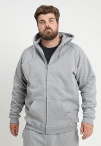 Sudadera gris con cremallera, hecha de material tipo sudadera, que presenta una cremallera frontal, capucha ajustable y dos bolsillos frontales. Corte relajado con puños acanalados.