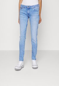 Jeans skinny de mezclilla azul claro con un diseño ajustado, cinco bolsillos, un ligero desgastado y costuras en contraste, combinados con zapatillas blancas.